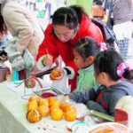 Kids watch as their mother explains how to puncture the orange to insert the cloves